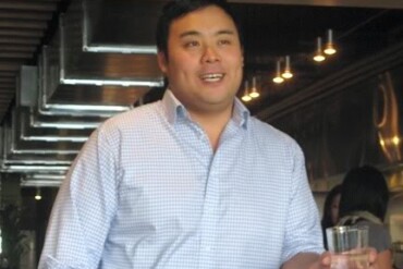 An Asian man leaning on a bar with a glass of water